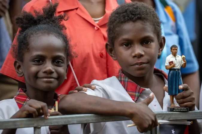 Two children, one of them holding a statue of Blessed Peter To Rot, await the visit of Pope Francis at the Caritas Technical Secondary School in Port Moresby, Papua New Guinea, Sept. 7, 2024