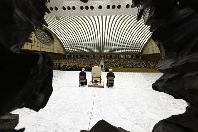 A view of Pope Francis addressing the faithful from the stage of the Vatican's Paul VI Audience Hall during the first Jubilee audience of 2025, seen through the distinctive carved stone entranceway.