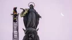 A firefighter scales a long ladder to the top of a nearly 40-foot-high column to pay tribute at dawn to the Blessed Virgin with a wreath of flowers on Dec. 8, 2023. | Credit: Daniel Ibanez/CNA