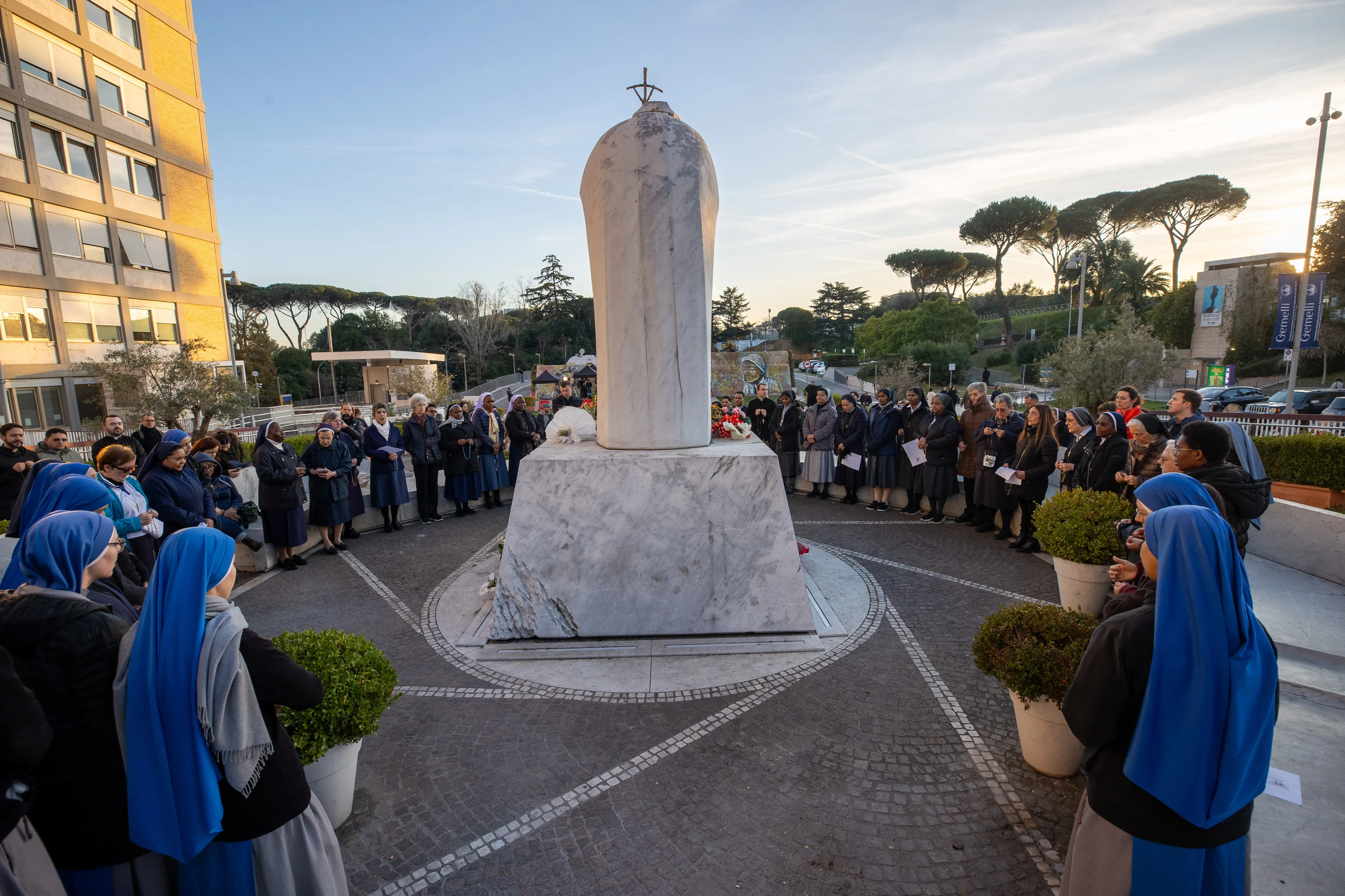 Religious sisters and faithful gather around the statue of St. John Paul II at Gemelli hospital to pray the rosary for Pope Francis on Saturday aftern