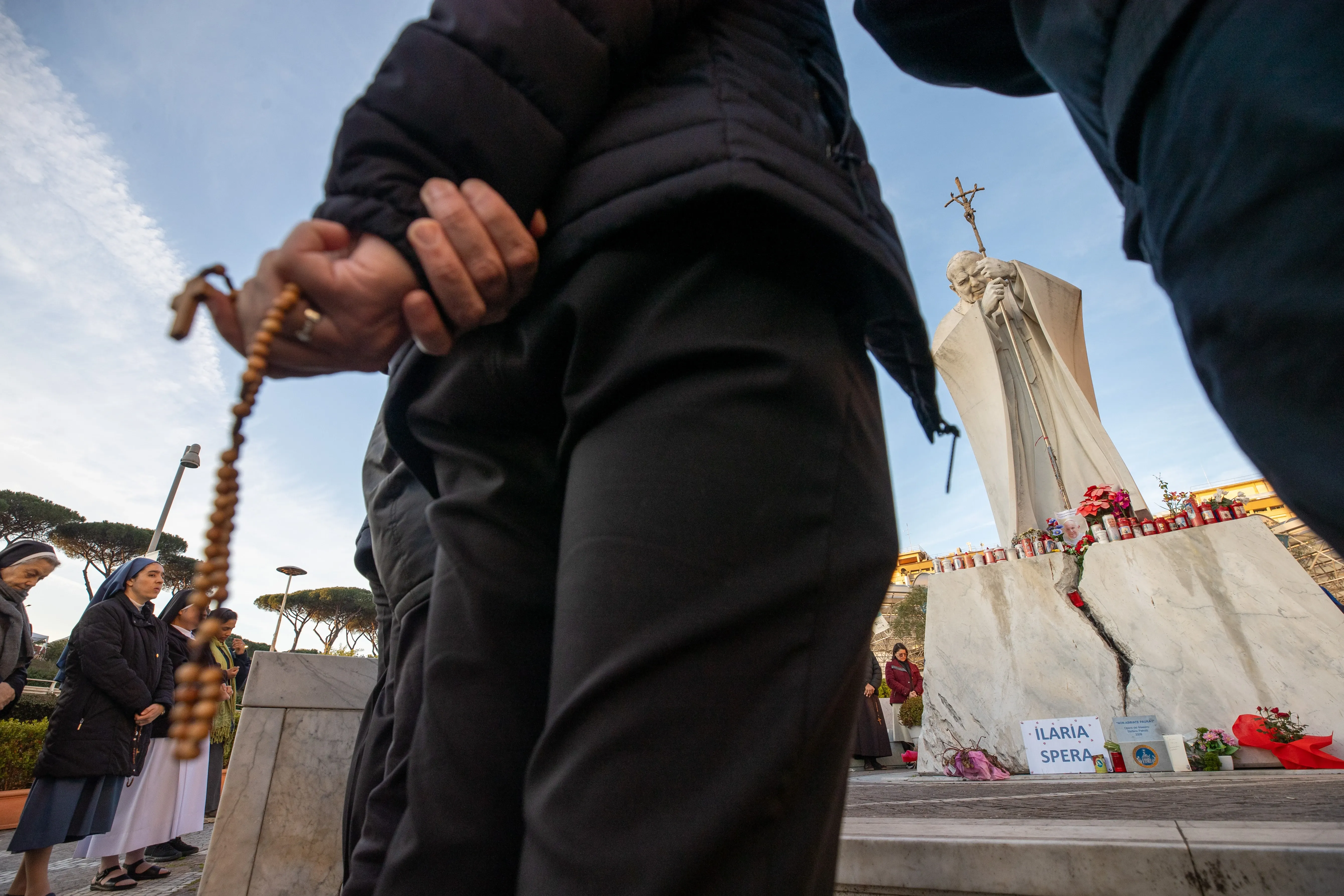 A faithful holds a rosary while praying for Pope Francis near the statue of St. John Paul II outside Gemelli hospital on Saturday, Feb. 22, 2025